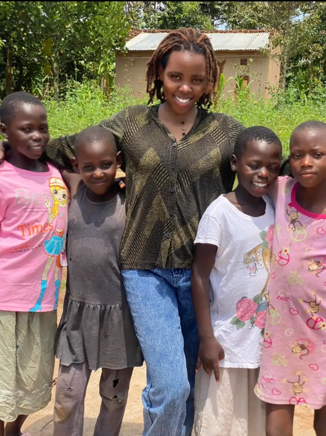 A smiling woman standing with young girls from Busoga region as part of the SheBloom empowerment initiative